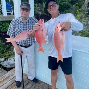 two senior men outdoors holding up red snapper fish