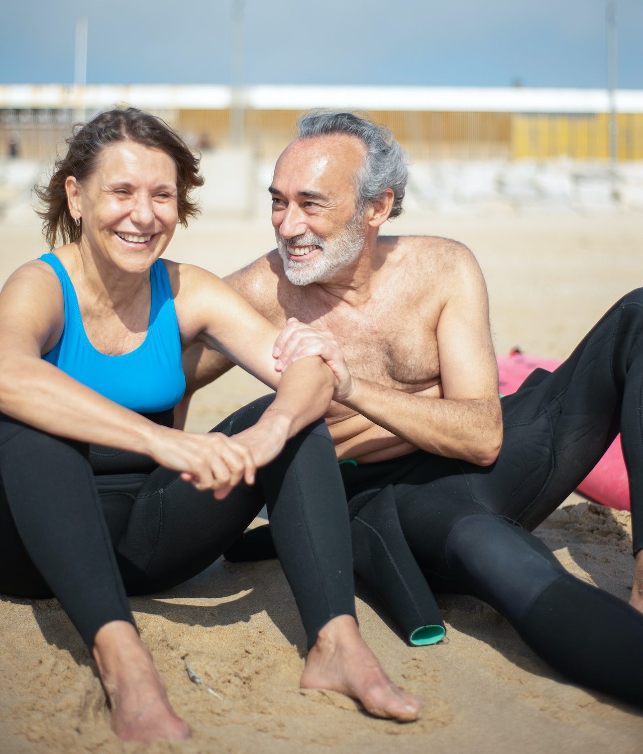 senior man and woman on sunny beach in wetsuits